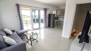 Un salon moderne avec un canapé, une table basse en verre et une porte-fenêtre coulissante donnant sur un balcon.