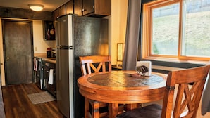 A compact kitchen with a refrigerator, wooden dining table, chairs, and a window with a view of the outdoors. - Cozy 1 Bedroom, Sleeps 3, Steps from Shuttle! Hot Tub! Loved by guests! (Crested Butte)