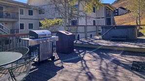 A deck with a grill, a table, and chairs, surrounded by buildings and trees. - Cozy 1 Bedroom, Sleeps 3, Steps from Shuttle! Hot Tub! Loved by guests! (Crested Butte)