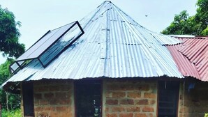 Une petite maison en briques, avec un toit en tôle ondulée, une fenêtre et une porte.