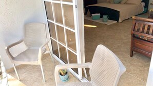 Ein Schlafzimmer mit einem Bett, zwei Stühlen und einer Glastür, die zu einem Außenbereich mit einem Blumentopf führt.