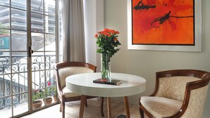 Ein Zimmer mit einem runden Tisch, zwei Stühlen, einer Vase mit Blumen, einem Buch und einem Gemälde an der Wand.