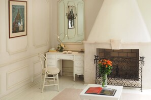 A room with a white desk, a chair, a book, a vase with flowers, and a fireplace.