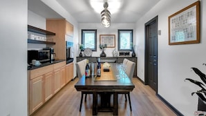 A modern kitchen with wooden cabinets, a black countertop, and a dining area with a wooden table and chairs. - King Estate with attached Mid-Century Apartment & Gym. (Wichita)