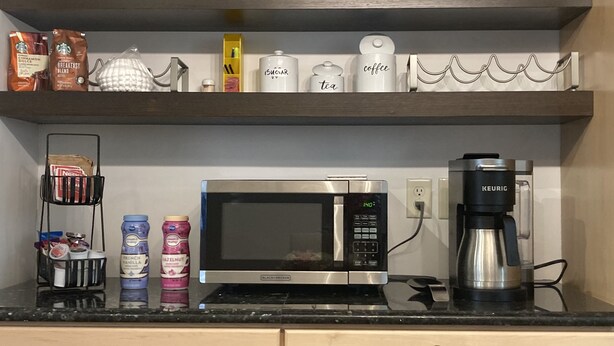 Keittiössä on mikroaaltouuni, kahvinkeitin sekä hyllyjä, joilla on kahvikuppeja, sokeria ja teetä.