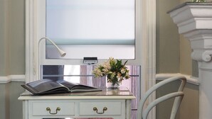 Een wit bureau met een stoel, een raam en een vaas met bloemen.