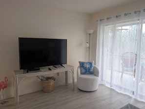 Un salon avec un téléviseur posé sur un meuble, un fauteuil avec un coussin, une lampe et une fenêtre donnant sur un beau paysage.