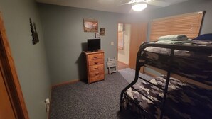 A bedroom with a bunk bed, a wooden dresser, a ceiling fan, and a door leading to another room. - 2-bedroom vacation home sitting on your own private lake for fishing/relaxing. (Howard)