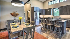Une cuisine moderne avec des meubles de couleur sombre, des appareils en acier inoxydable et un coin repas avec des chaises en bois et une table dressée pour deux personnes.