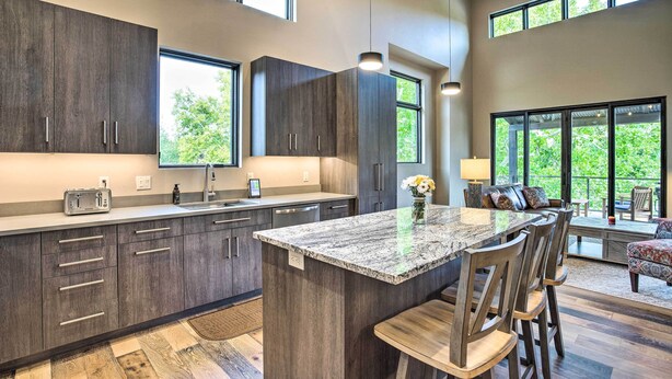 Une cuisine moderne avec des meubles de couleur sombre en bois, un îlot central en granit et une grande fenêtre donnant sur un espace verdoyant.