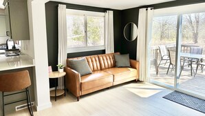 A modern living room with a leather sofa, a dining area with a table and chairs, and a kitchen area with a counter and appliances. - Orchard Ranch - Fish Creek | Sleeps 10 • Trails • Coffee Bar • Snowshoes (Fish Creek)