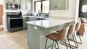 A modern kitchen with a central island, stainless steel appliances, and light green cabinetry. - Orchard Ranch - Fish Creek | Sleeps 10 • Trails • Coffee Bar • Snowshoes (Fish Creek)