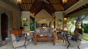 A spacious living area with a high ceiling, a central sofa, and a coffee table. There is a kitchen in the background, and the room has a tropical theme with plants and a view of the outdoors. - Spacious, 800sqm, Pool and Garden Retreat, Sanur Village (Sanur)