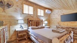 Une chambre dans une cabane en bois, avec un lit, deux tables de chevet, une lampe et un téléviseur fixé au mur.