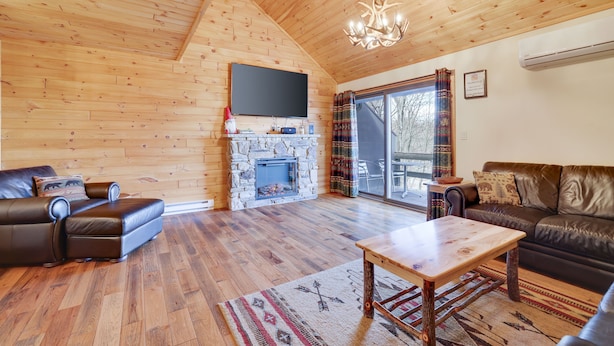 Un salon chaleureux avec une cheminée en pierre, des canapés en cuir, un plafond en bois et une grande fenêtre.