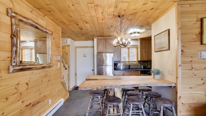 Un intérieur en bois avec un îlot central, des tabourets de bar, un lustre et un espace cuisine.