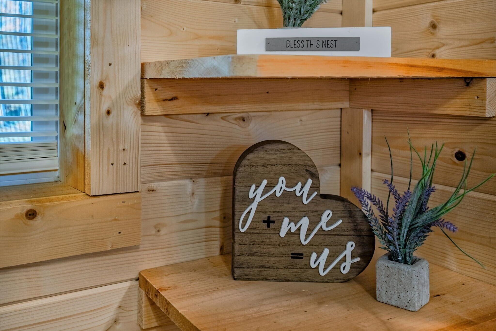 A wooden shelf with a sign that reads "Bless This Nest" and a decorative sign that says "you + me = us".