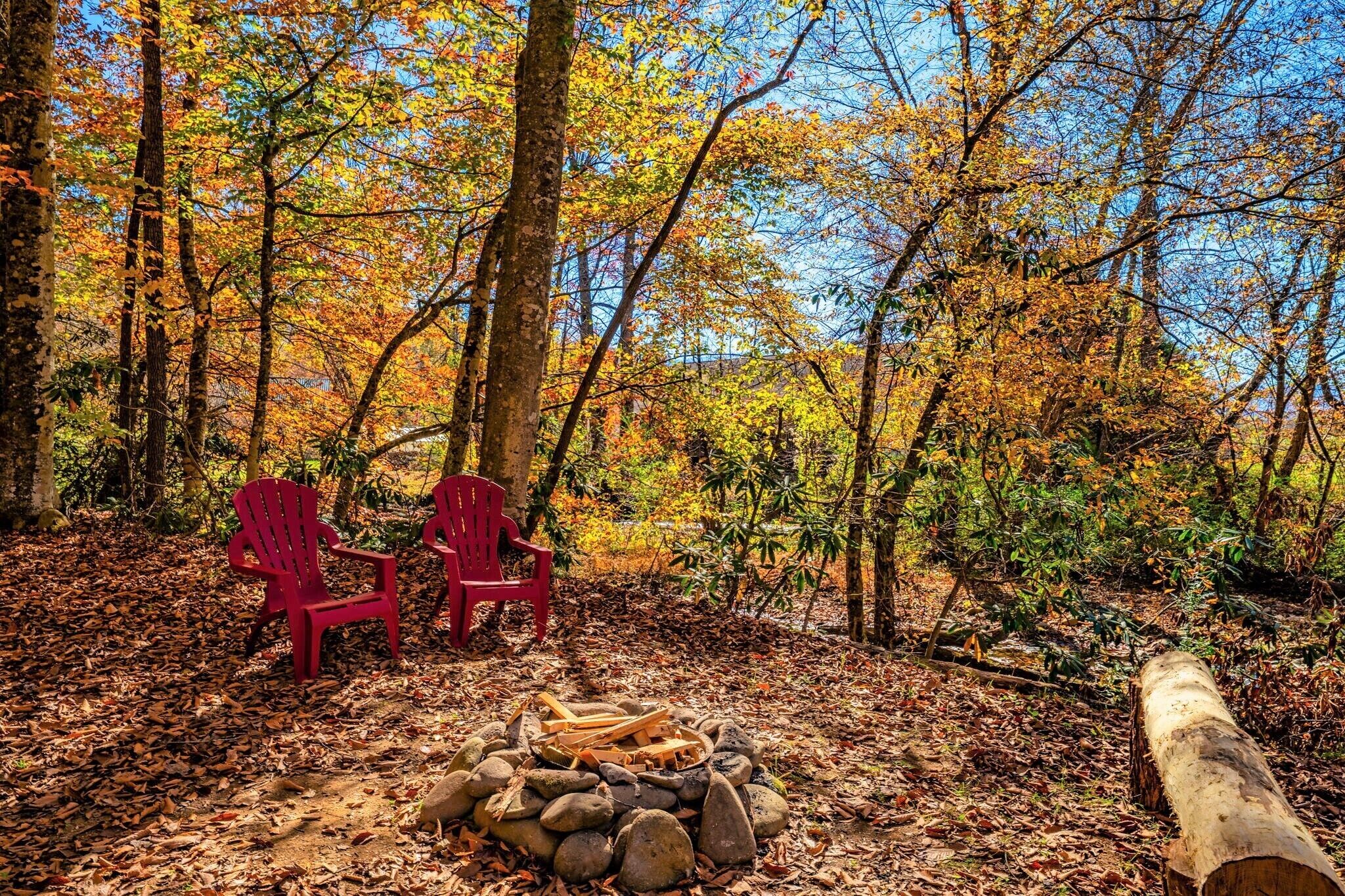 A forest scene with two red chairs and a fire pit.