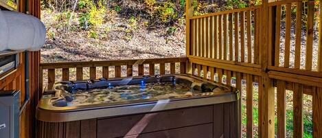 Un jacuzzi en una terraza de madera con vistas a un bosque.
