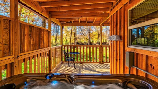 A wooden deck with a hot tub, a table, and chairs, surrounded by a wooden fence and trees. - Cuddling On The Creek Couples only romantic " TINY CABIN" retreat!!!! (Cosby)