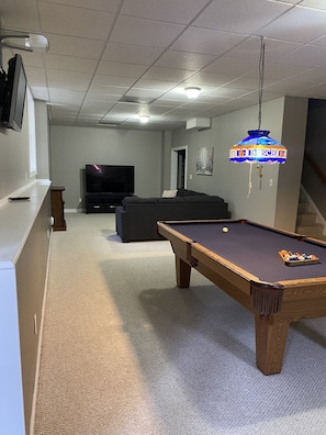 Ein Wohnzimmer mit Poolbillardtisch, einer Couch, einem Fernseher und einem Chandelier.