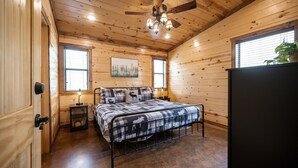 Quarto com painéis de madeira, uma cama, ventilador de teto e janela com persianas.