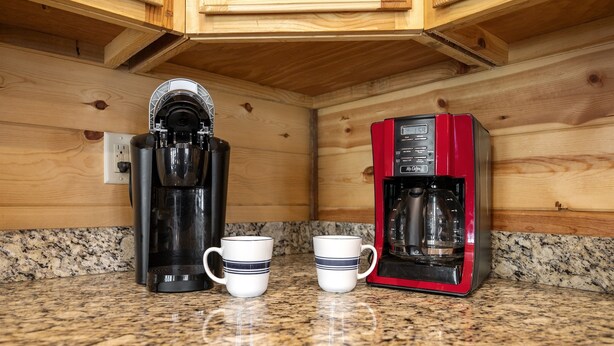 A kitchen with two coffee makers, two white mugs with blue stripes, and a granite countertop.