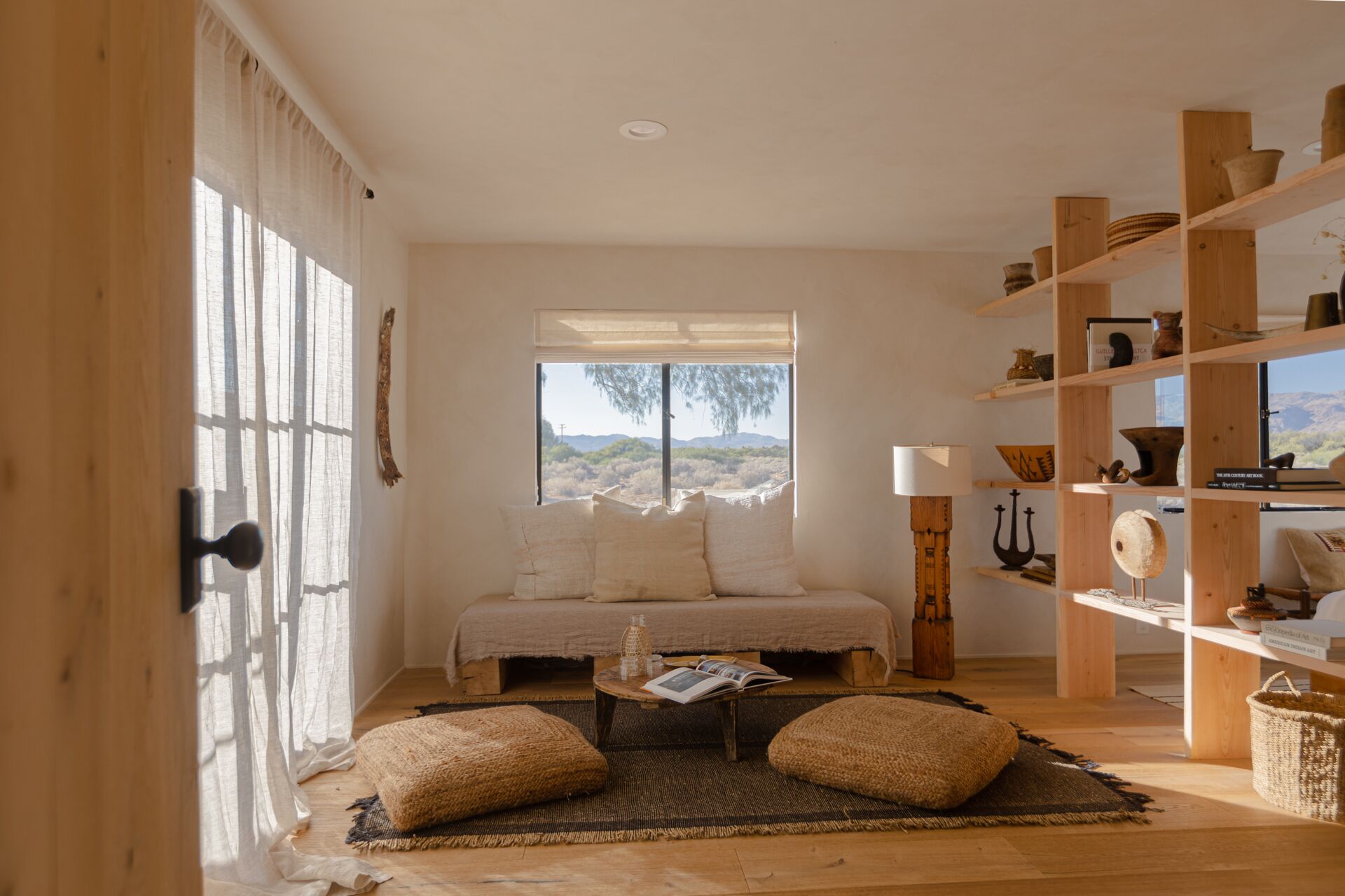 Un dormitorio acogedor con un ventanal grande, una estantería de madera y una mesita de noche.