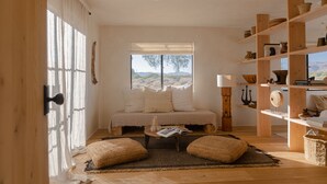 A cozy bedroom with a large window, a wooden bookshelf, and a bedside table.