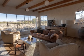 A spacious living room with a leather couch, a glass coffee table, and a view of a desert landscape through large windows.