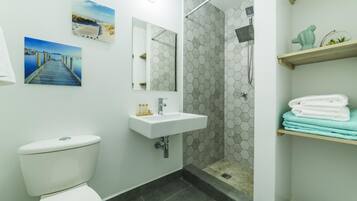 Un bagno con WC, lavandino, doccia e uno scaffale con asciugamani.