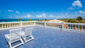 A terrace with two white chairs and a small table, overlooking a coastal view with a clear sky.