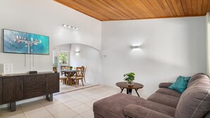 Una sala moderna con techo de madera, un sofá marrón, un comedor con sillas de madera y un televisor montado en la pared.