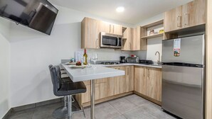 Une cuisine moderne avec des meubles en bois, un réfrigérateur en acier inoxydable, un four à micro-ondes et un téléviseur à écran plat fixé au mur.