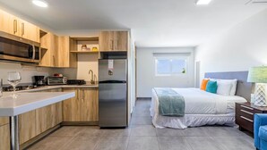 Une cuisine compacte dotée d’appareils électroménagers modernes, un coin repas et une chambre avec un grand lit et des coussins colorés.