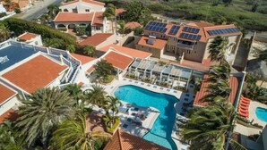 Eine Luftaufnahme eines Resorts mit Schwimmbad, Solaranlagen und Palmen.
