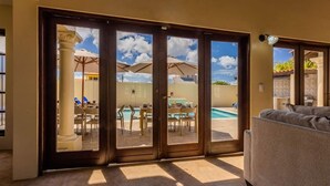 Une pièce dotée d’une porte-fenêtre coulissante donnant sur un espace piscine équipé de parasols et de chaises.