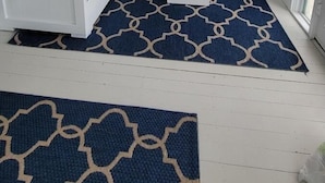 A room with a blue sofa, white coffee table, and a patterned rug. There is a window with a view of houses outside.
