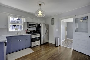 A modern kitchen with grey cabinets, stainless steel appliances, a wooden floor, and a chandelier.
