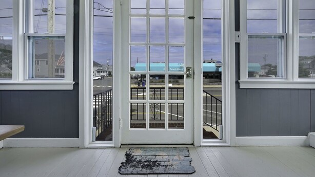 A room with a white door, two windows, and a view of a building with a blue roof.