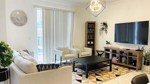 Un salon moderne comprenant un canapé, deux fauteuils, une table basse, un téléviseur et une bibliothèque.