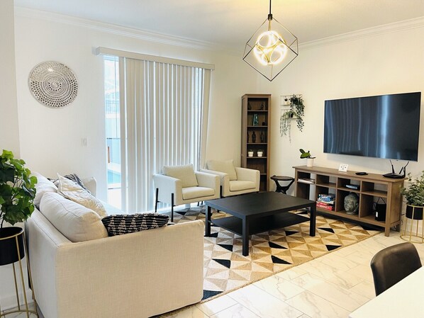 Una sala de estar moderna con un sofá, dos sillones, una mesa de centro, un televisor y una estantería.