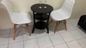 Une petite table ronde, avec deux chaises blanches et deux verres à vin posés dessus.