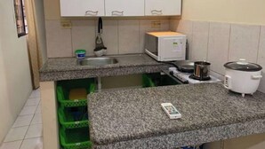 Une cuisine compacte équipée d’un four à micro-ondes, d’une cuisinière et d’un évier. On y trouve des bacs de rangement verts sous le plan de travail et un petit réfrigérateur.