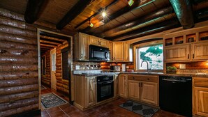 Cocina de cabaña de troncos con armarios de madera, estufa, microondas y lavavajillas.