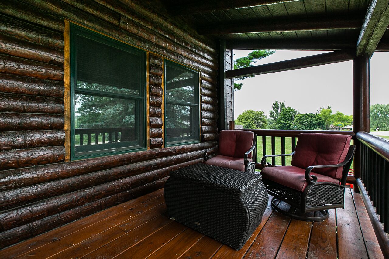 A log cabin with a wooden deck, two wicker chairs, and a wicker ottoman.
