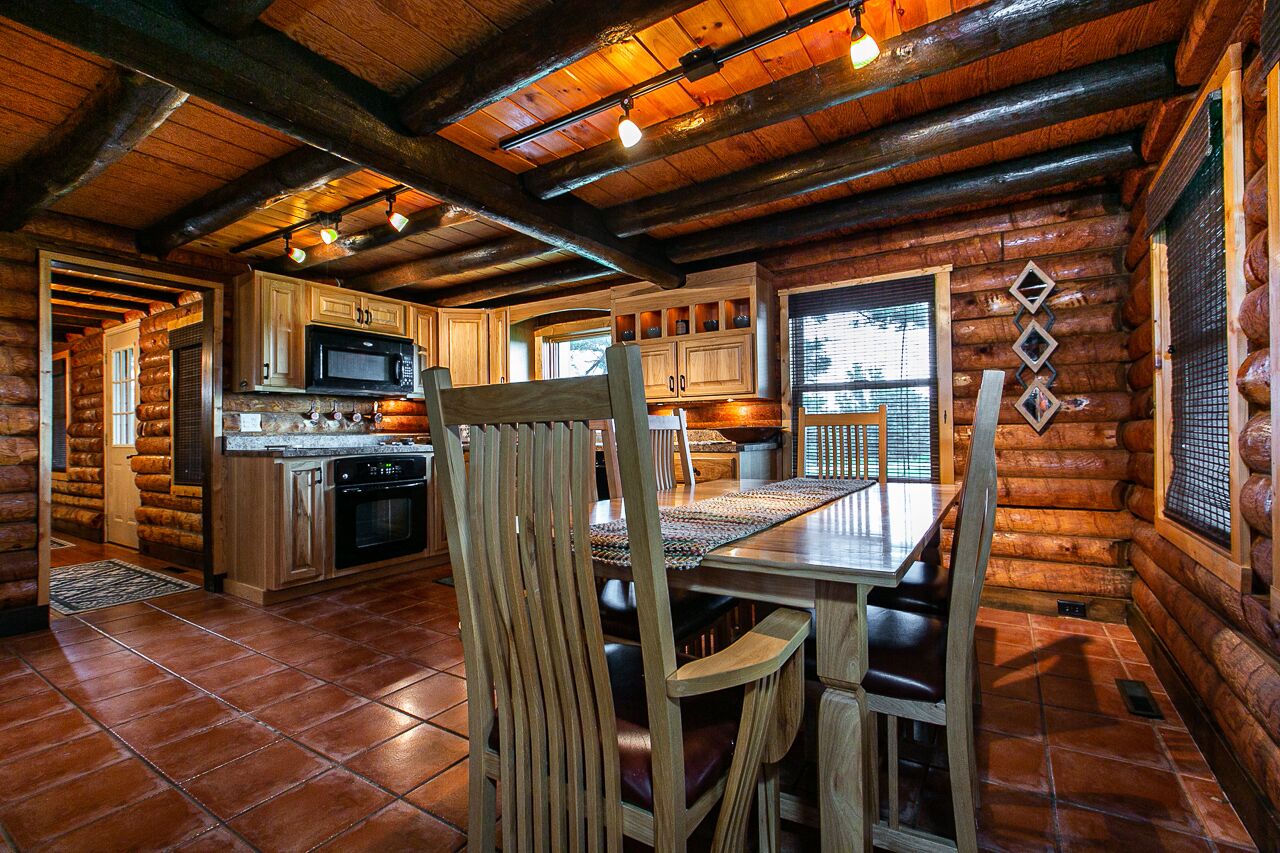 Interior de una cabaña de troncos con cocina, comedor y un amplio ventanal.