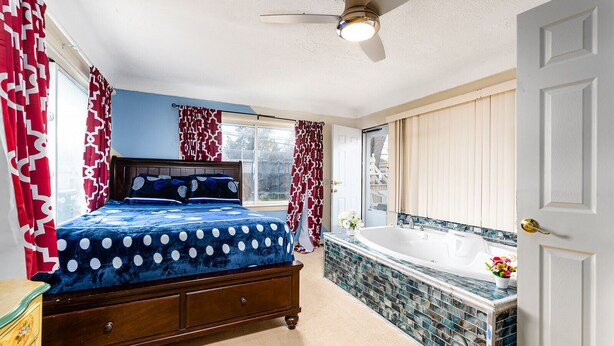 A bedroom with a large bed, a bathroom with a bathtub, and a ceiling fan. - Luxe 7 bdr 4 Fullbath with Jacuzzi on West side Detroit (Detroit)