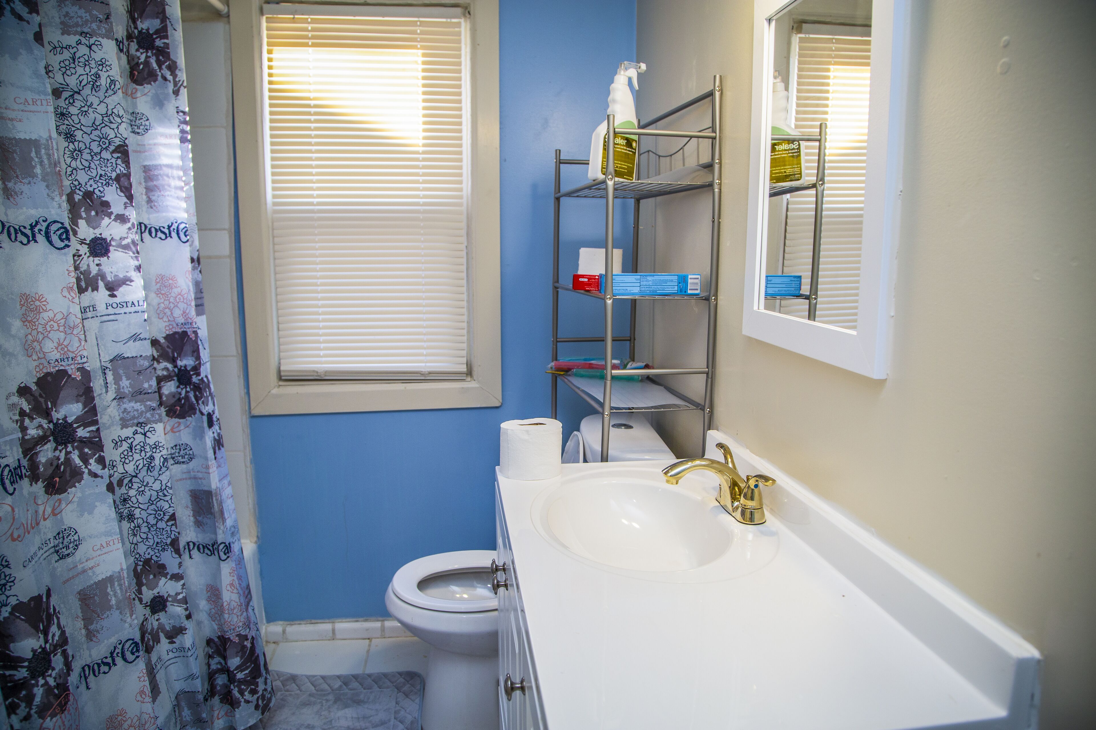 A bathroom with a toilet, sink, and shelves with toiletries.