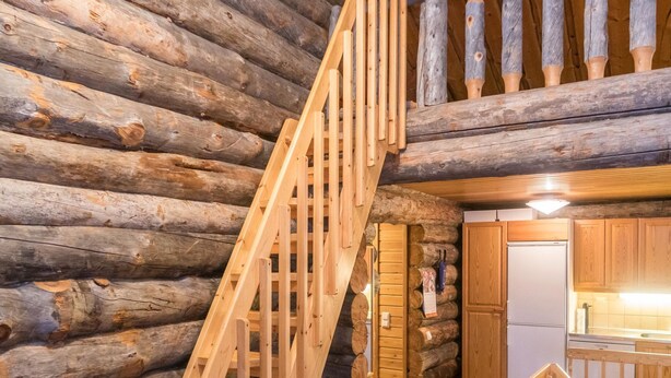 A log cabin interior with a wooden staircase leading to a loft area.
